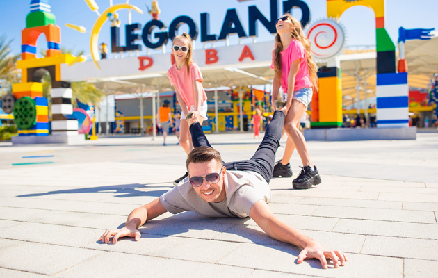 Daughters dragging father by legs who is laying on floor smiling to Legoland, Dubai